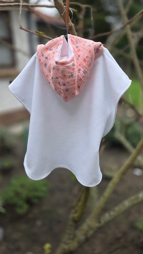 Small white hooded baby poncho towel with pink floral hood hanging on a tree branch outdoors.
