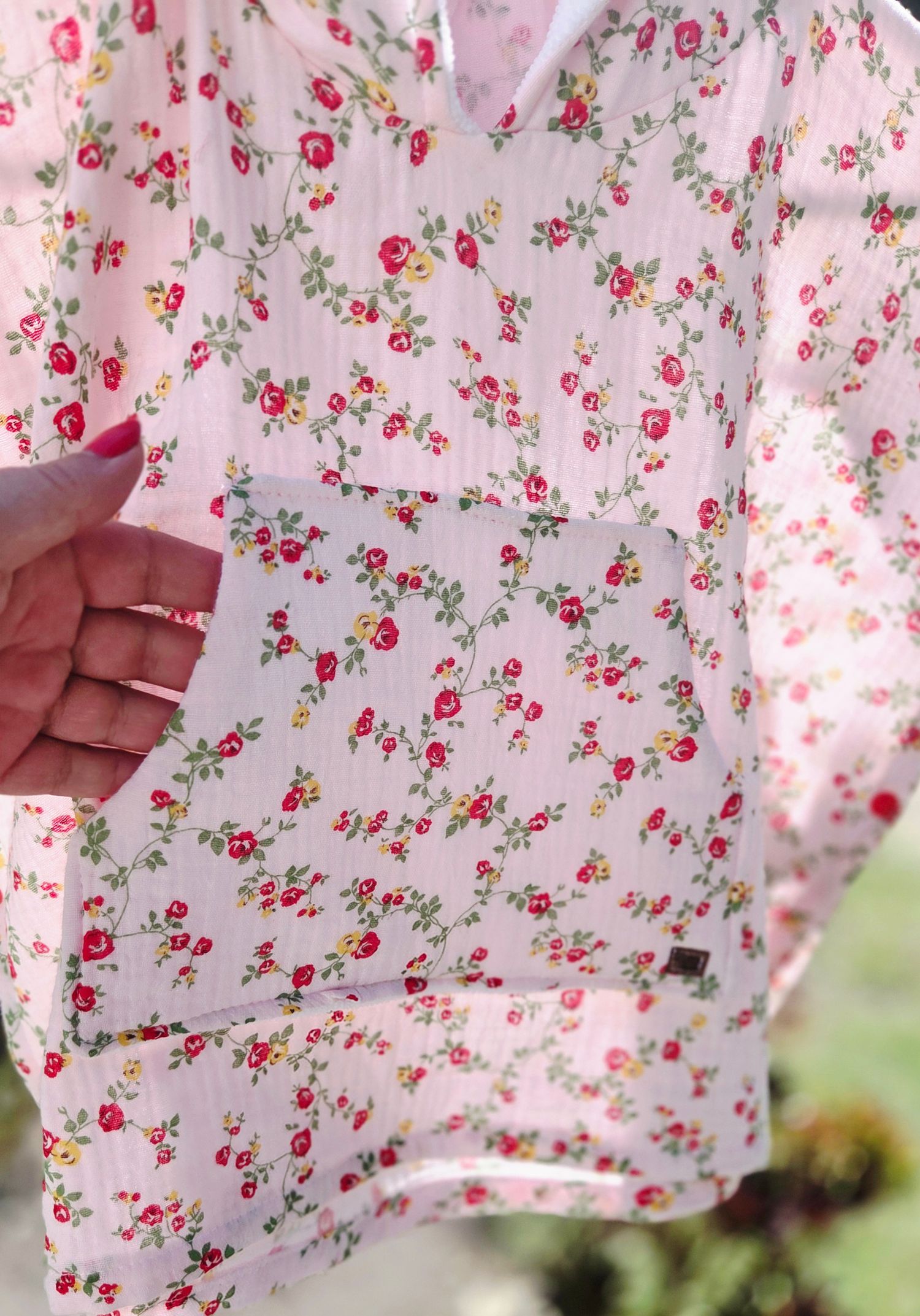Pink floral print blouse with red roses and green leaves pattern, held up by a hand with red nail polish.