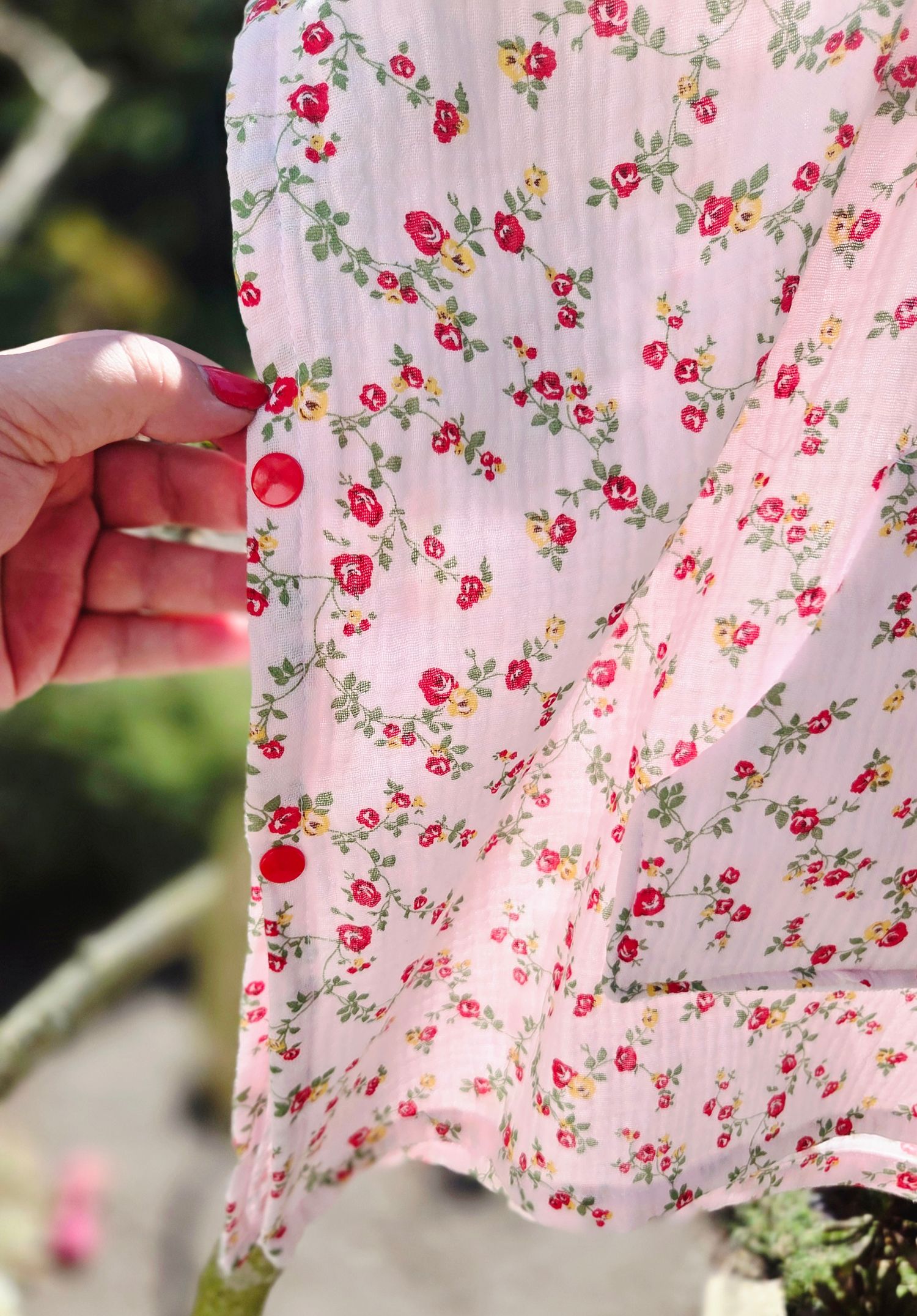 Hand holding pink floral fabric with red roses and green leaves pattern in soft natural light.