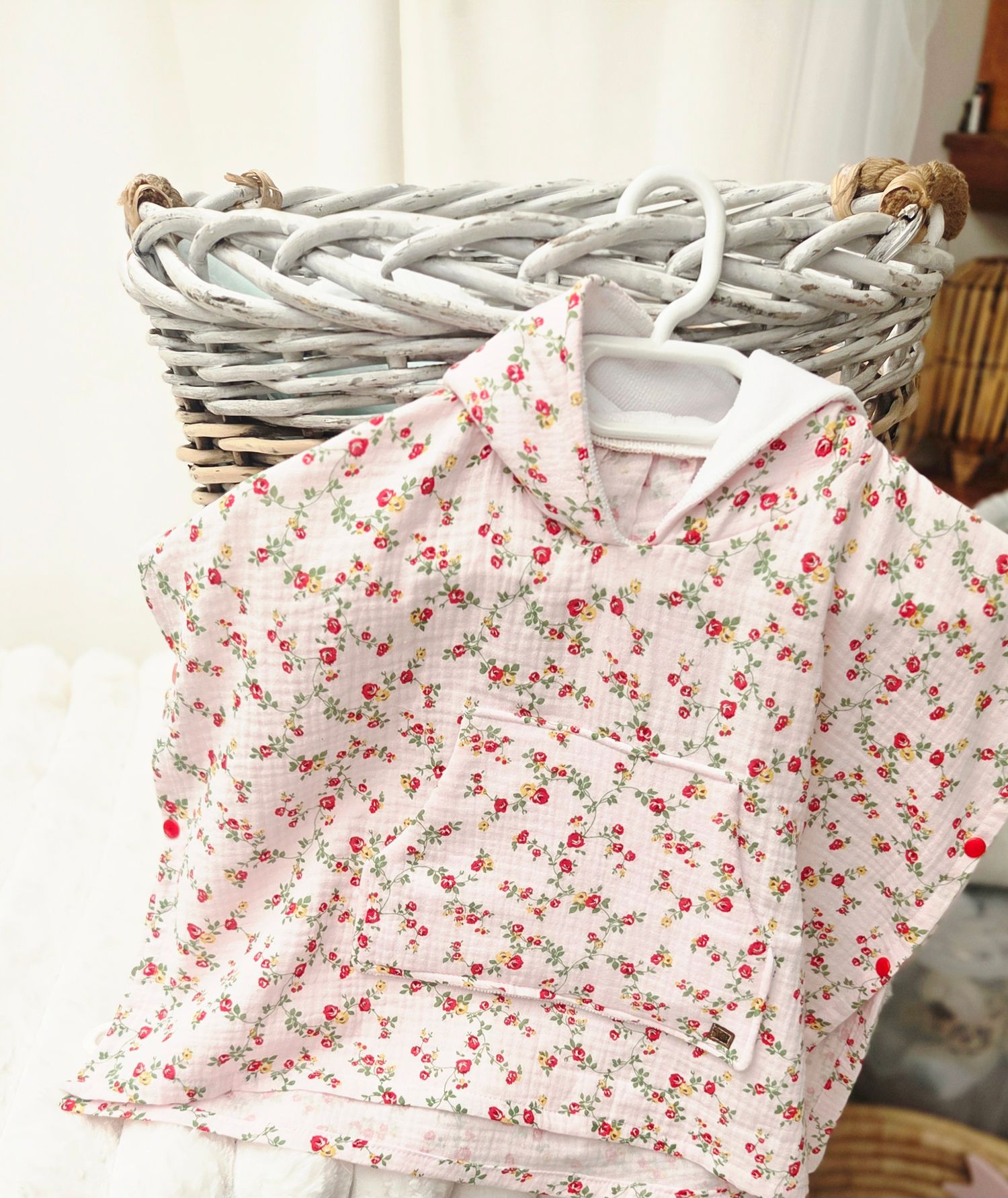 Pink floral hooded children's jacket on a white hanger, displayed against a woven wicker basket.