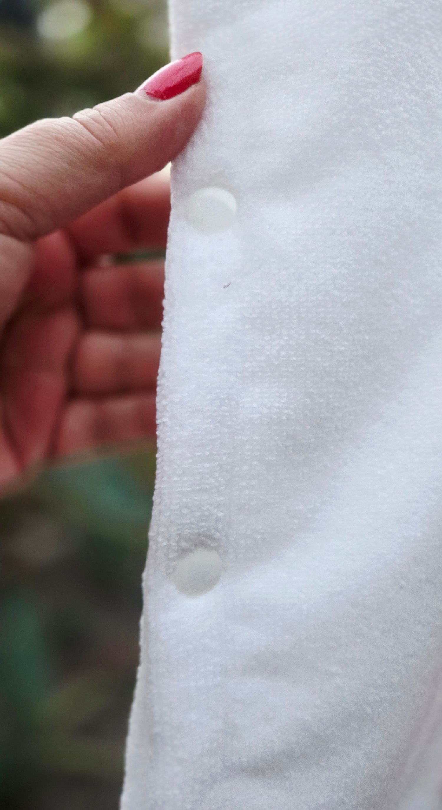 Close-up of a white fluffy robe with snap buttons, held open by a hand with red nail polish.