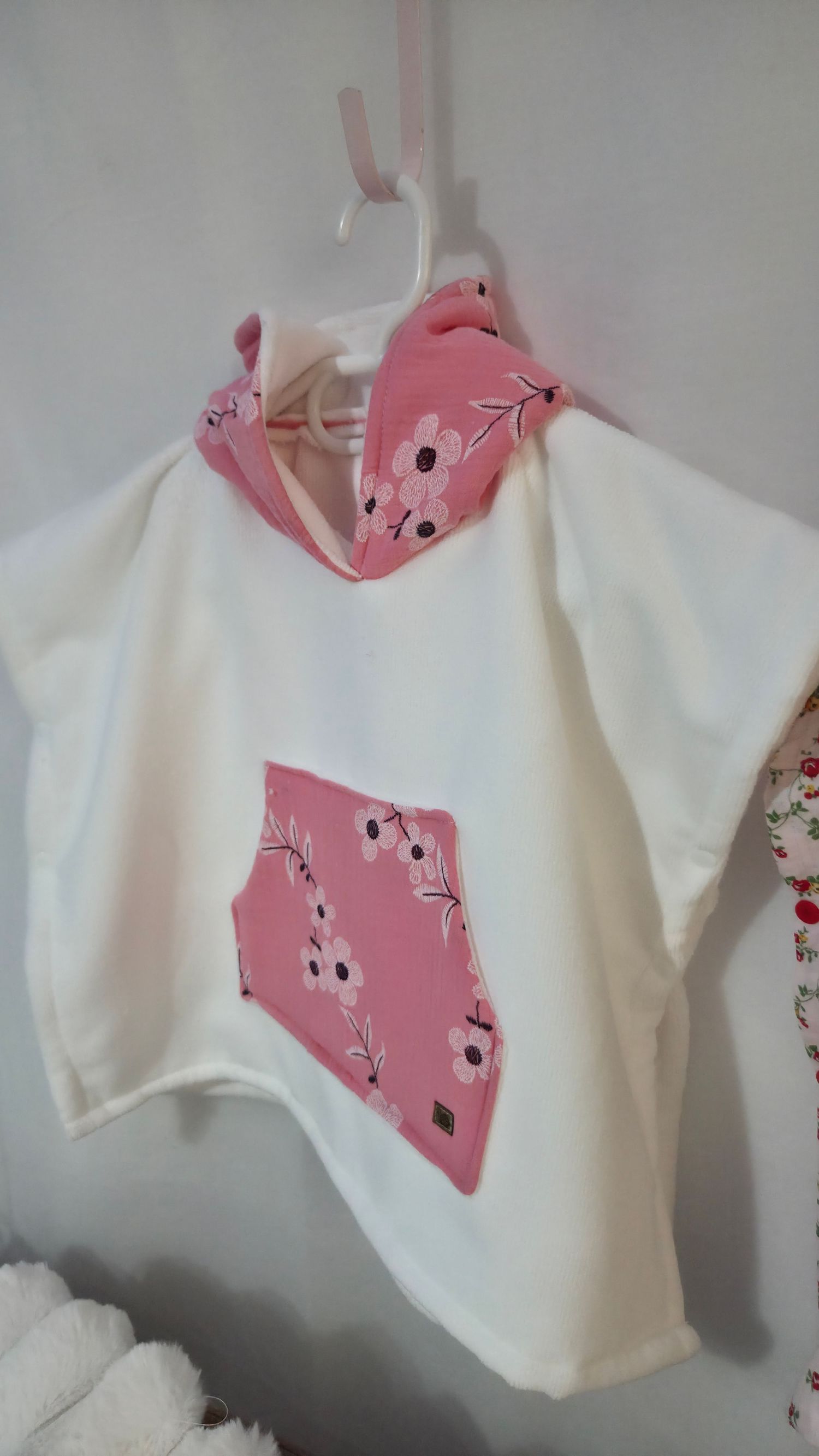 White children's hoodie with pink floral pocket and matching cowl neck collar hanging on a hanger.