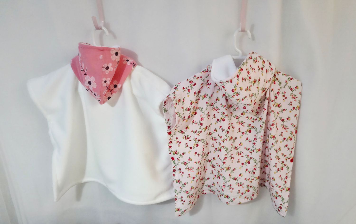 Two baby girls outfits on hangers, white bib top with pink scarf and floral print blouse with pink flowers.