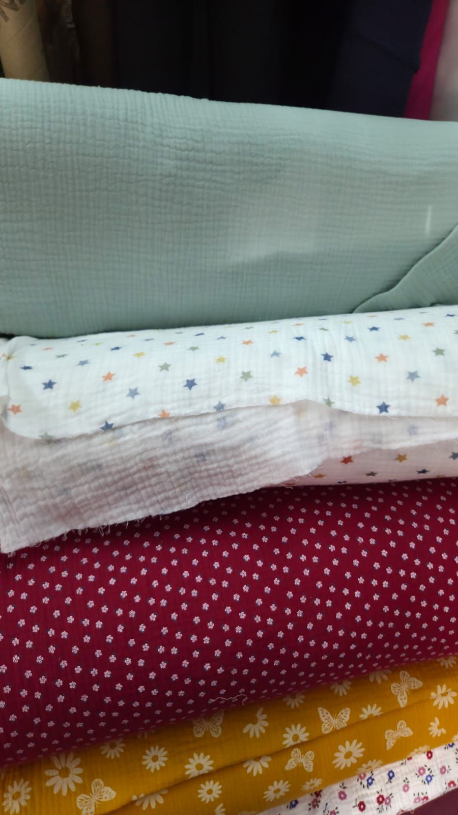 Stacked folded fabric bolts including mint green textured, white with colorful stars, pink, red floral, and yellow daisy prints.