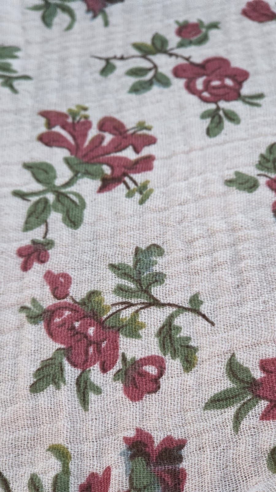 Vintage floral fabric with pink roses and green leaves on a white textured background.