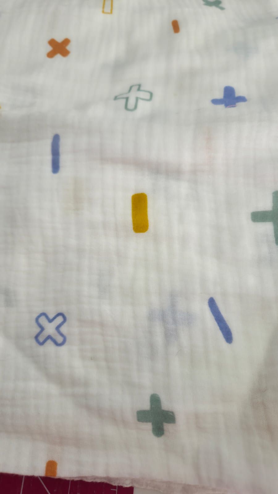 White muslin fabric with colorful plus signs, crosses, and dashes pattern in blue, green, orange, and yellow.