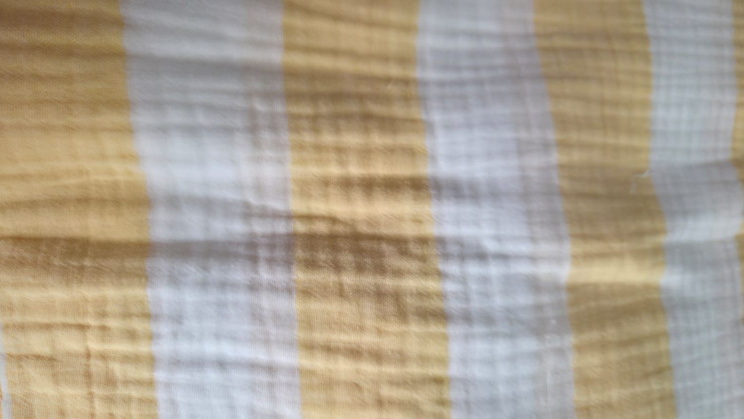 Close-up of soft muslin fabric with yellow, white, and gray plaid pattern, ideal for baby blankets or swaddles.