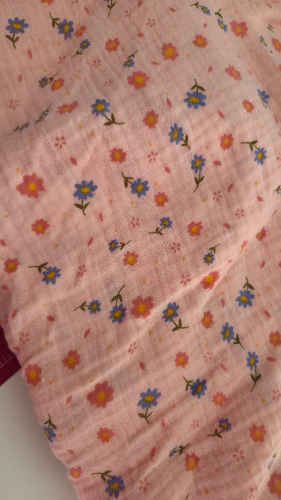 Pink floral muslin fabric with blue and orange daisy pattern, soft cotton textile for baby blankets or quilting projects.