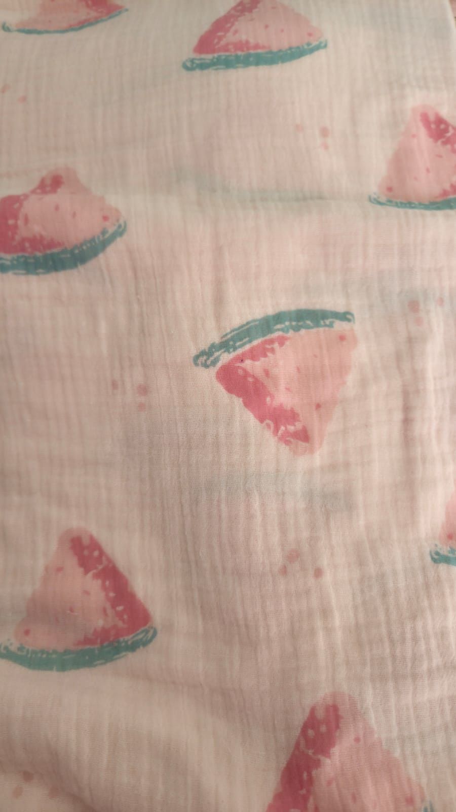 White muslin fabric with pink watermelon slice pattern and teal green accents, soft cotton swaddle blanket textile.
