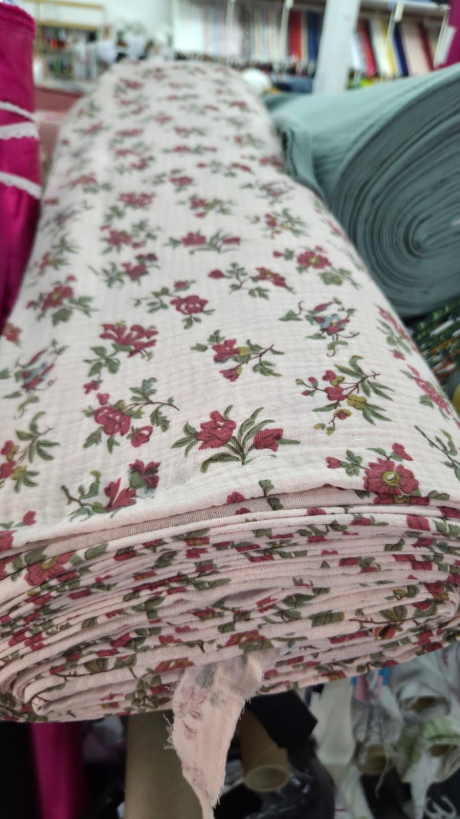 A rolled bolt of pink floral fabric with red roses and green leaves pattern, displayed in a fabric store.