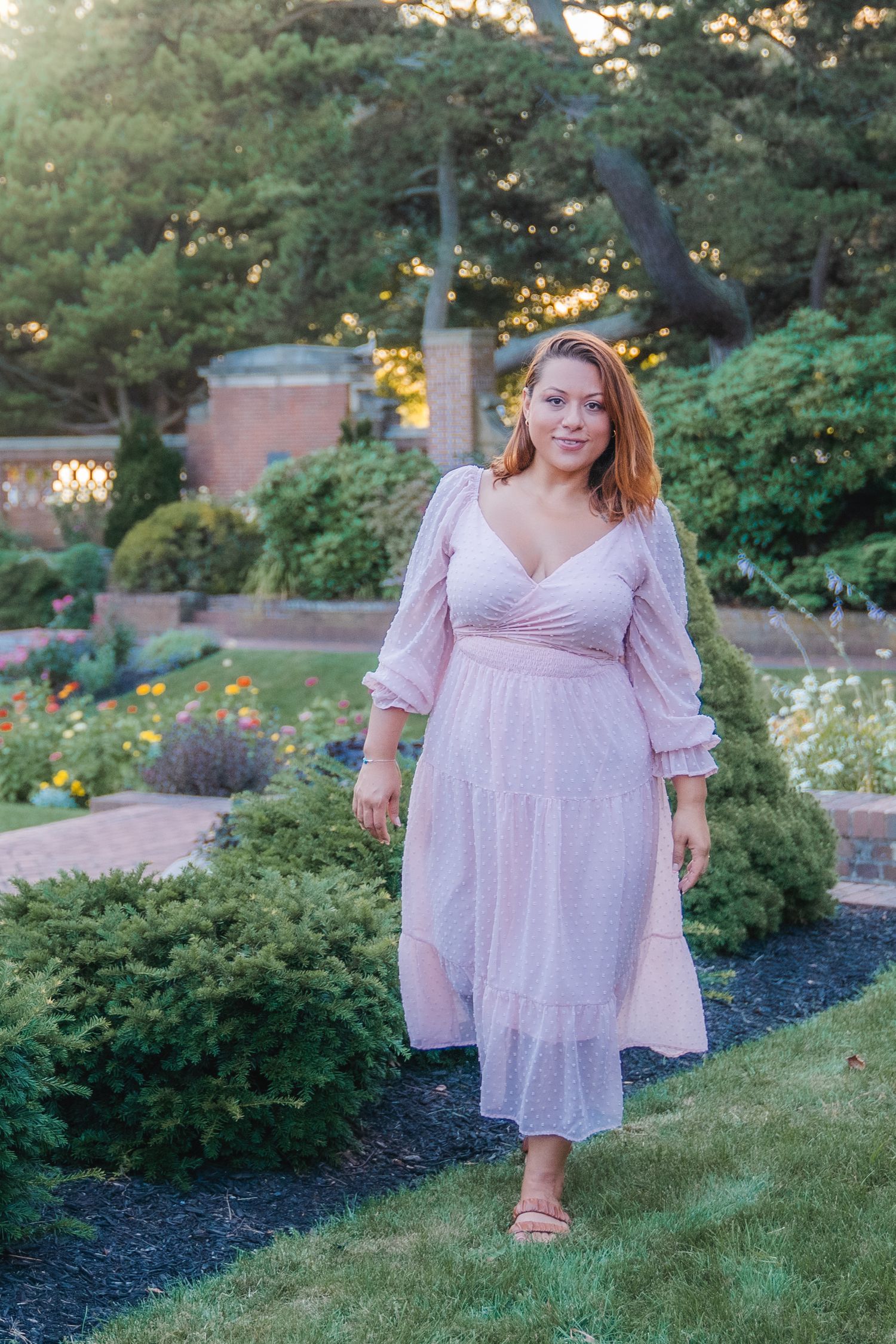 A garden portrait featuring a pink maxi dress against blooming flowers and green landscaping.