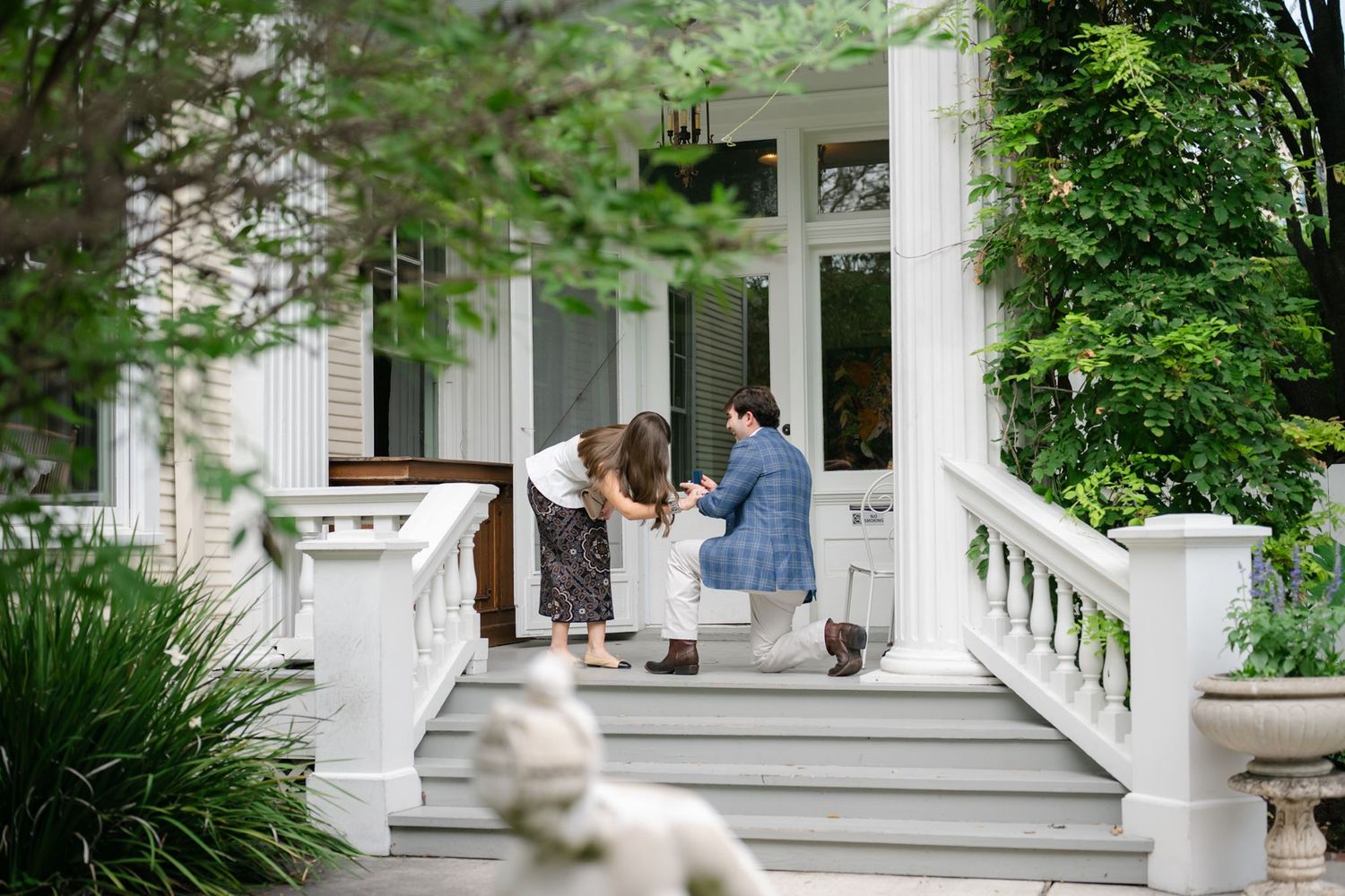 Man proposing to woman on a porch of a historic mansion.