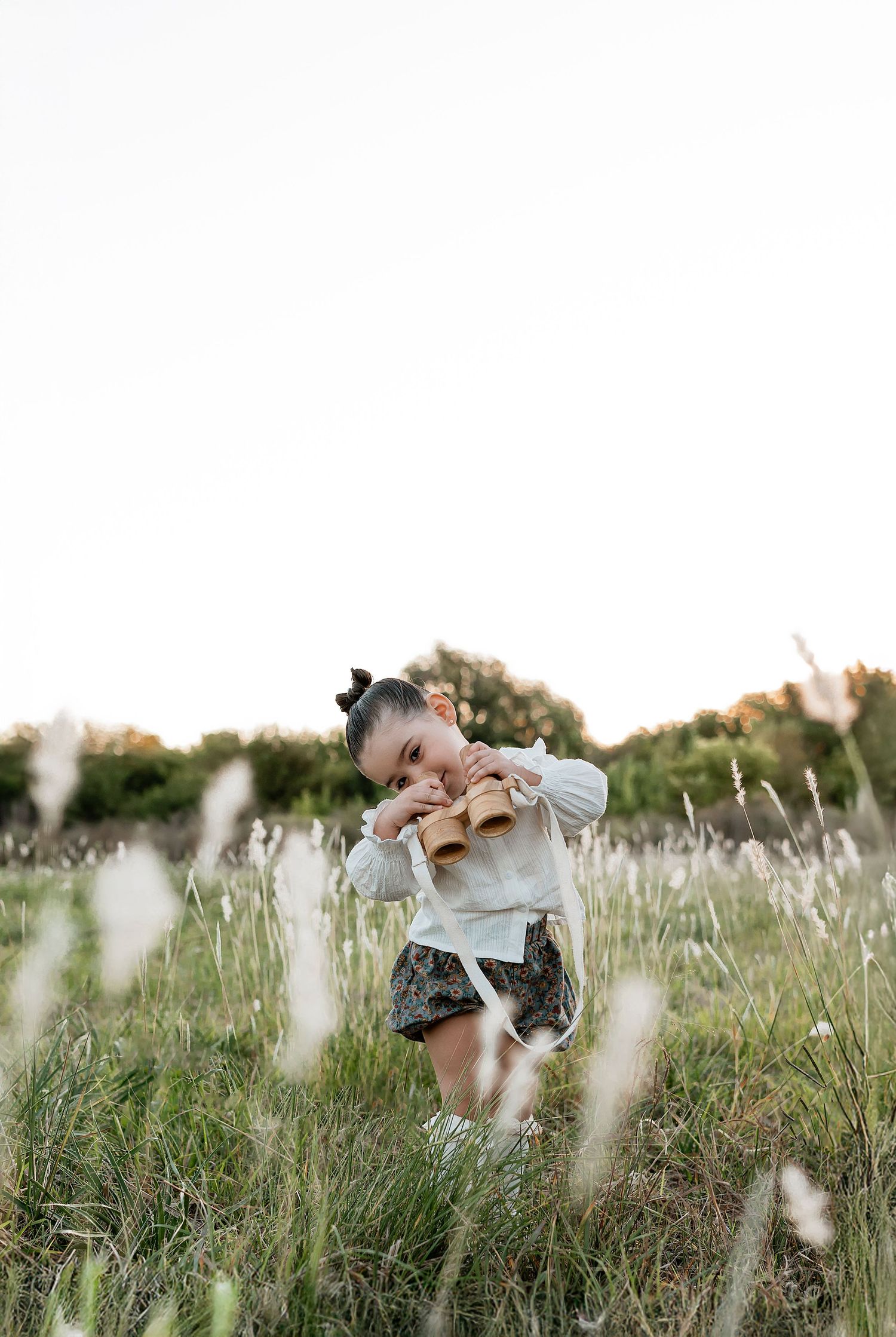 Young girl in white blouse and floral shorts playing in a wildflower meadow at golden hour.