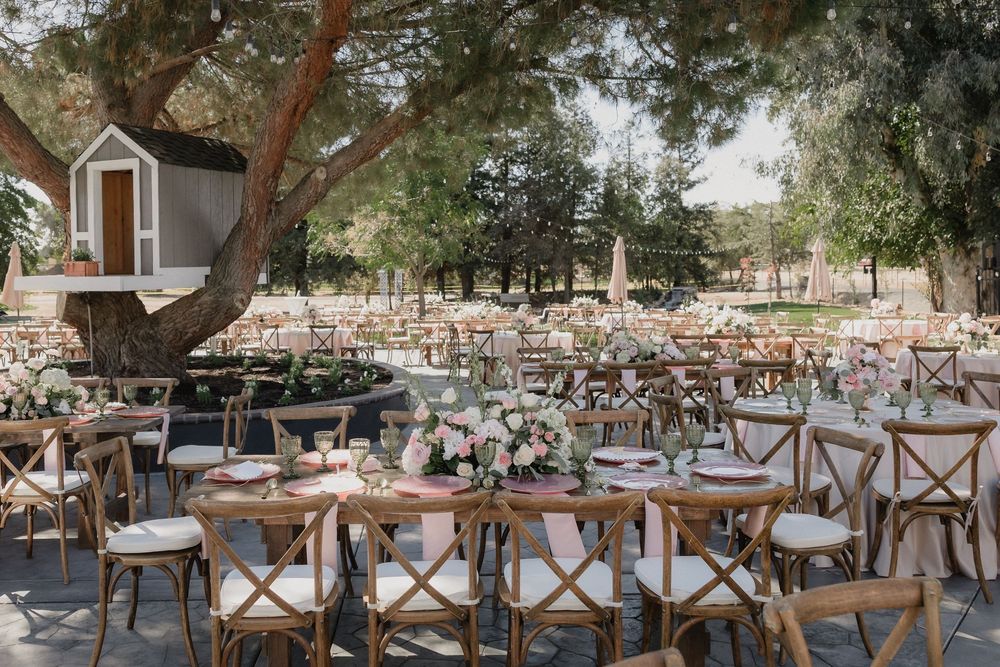 Elegant outdoor Quinceañera reception with rustic wooden chairs, round tables, and floral centerpieces.