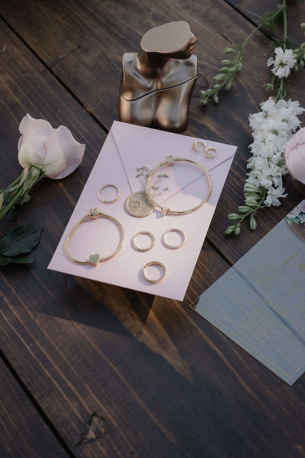 Elegant gold jewelry display with bracelets, rings, and earrings arranged on pink card with flowers.