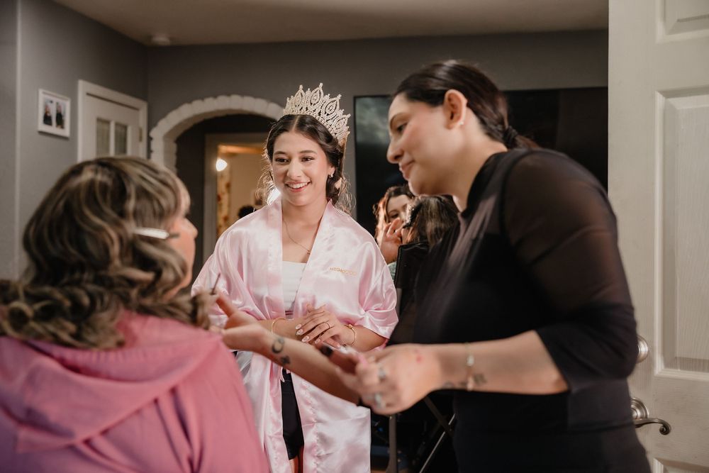 Quinceañera girl in pink satin robe and tiara smiling while getting ready with family members.