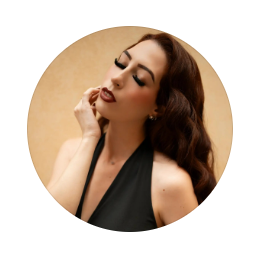 Woman with long dark wavy hair and bold red lipstick poses with eyes closed, hand near her face, wearing a black halter top.