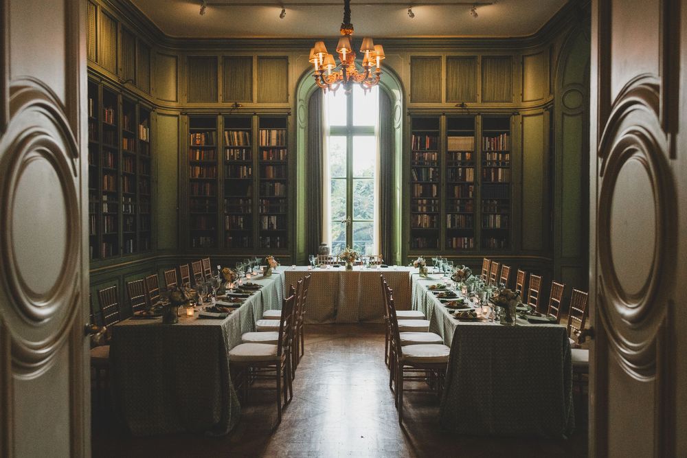 Elegant library dining room with floor-to-ceiling bookshelves, long set tables, and a chandelier for an intimate event at the Meridian House