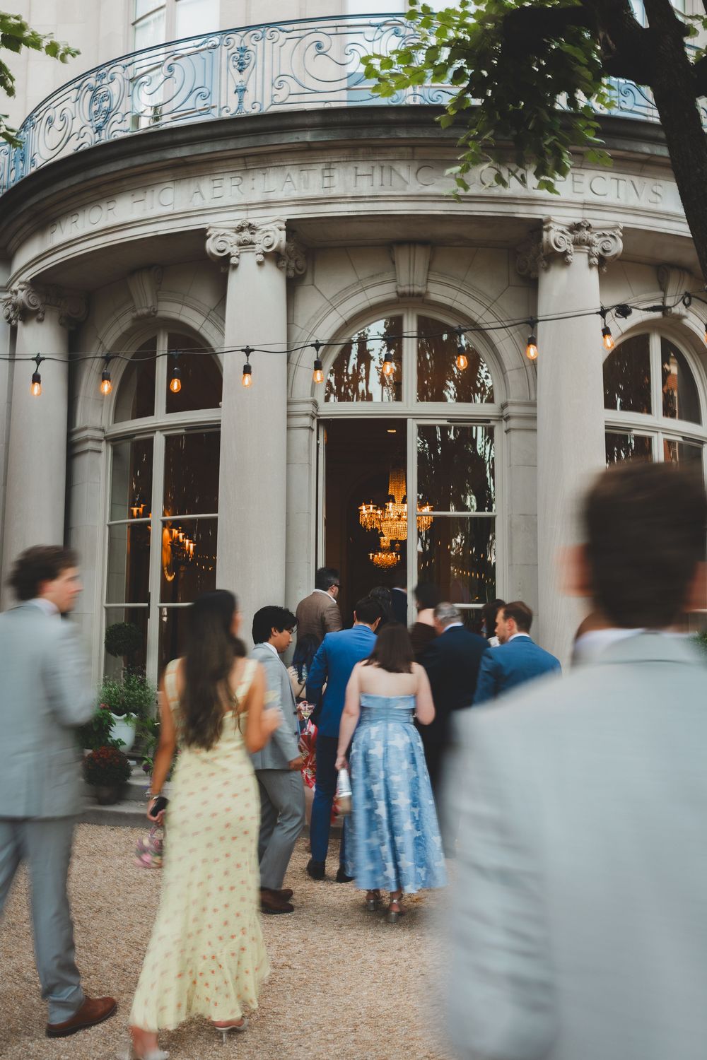 Elegantly dressed guests gather outside the meridian house dc with arched windows and string lights for a formal event.