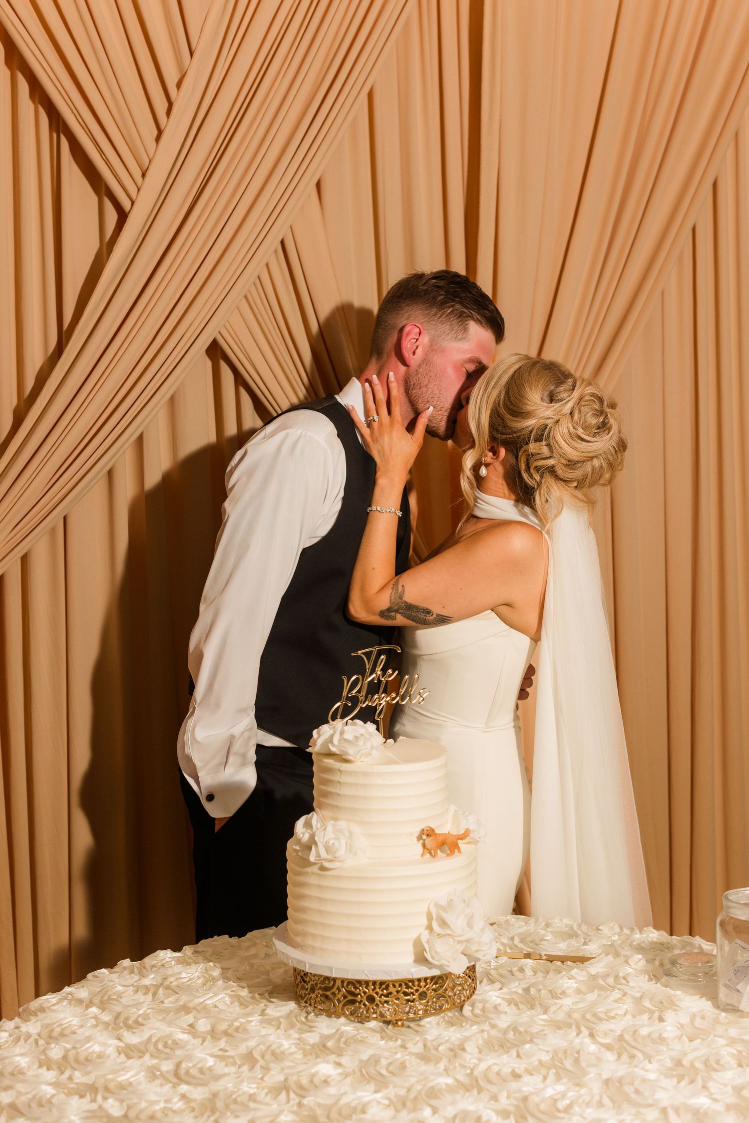 Bride and groom sharing a kiss behind a white tiered wedding cake at their elegant reception.