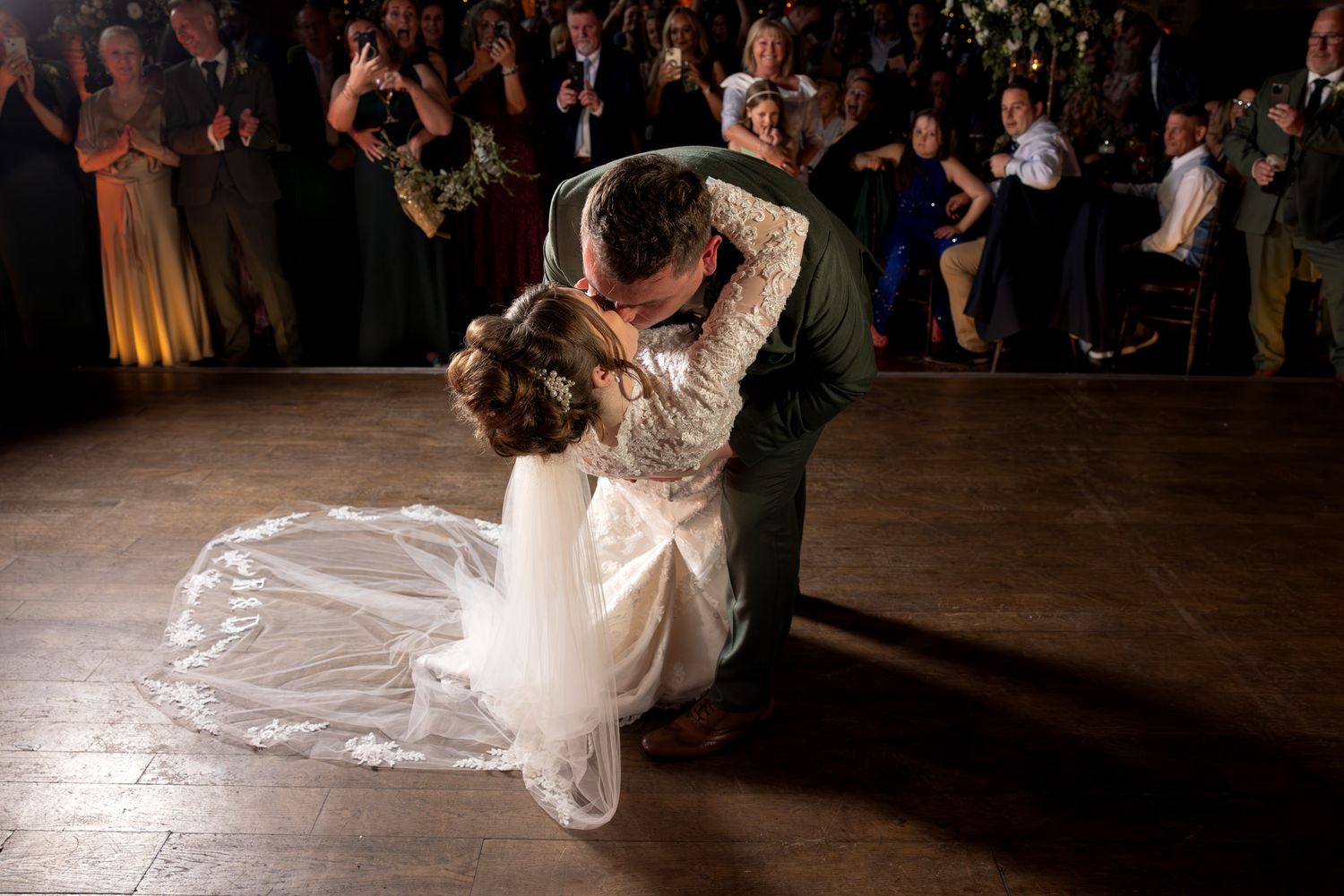 Groom dips his bride during their romantic first dance at Peckforton Castle, as wedding guests watch and applaud.