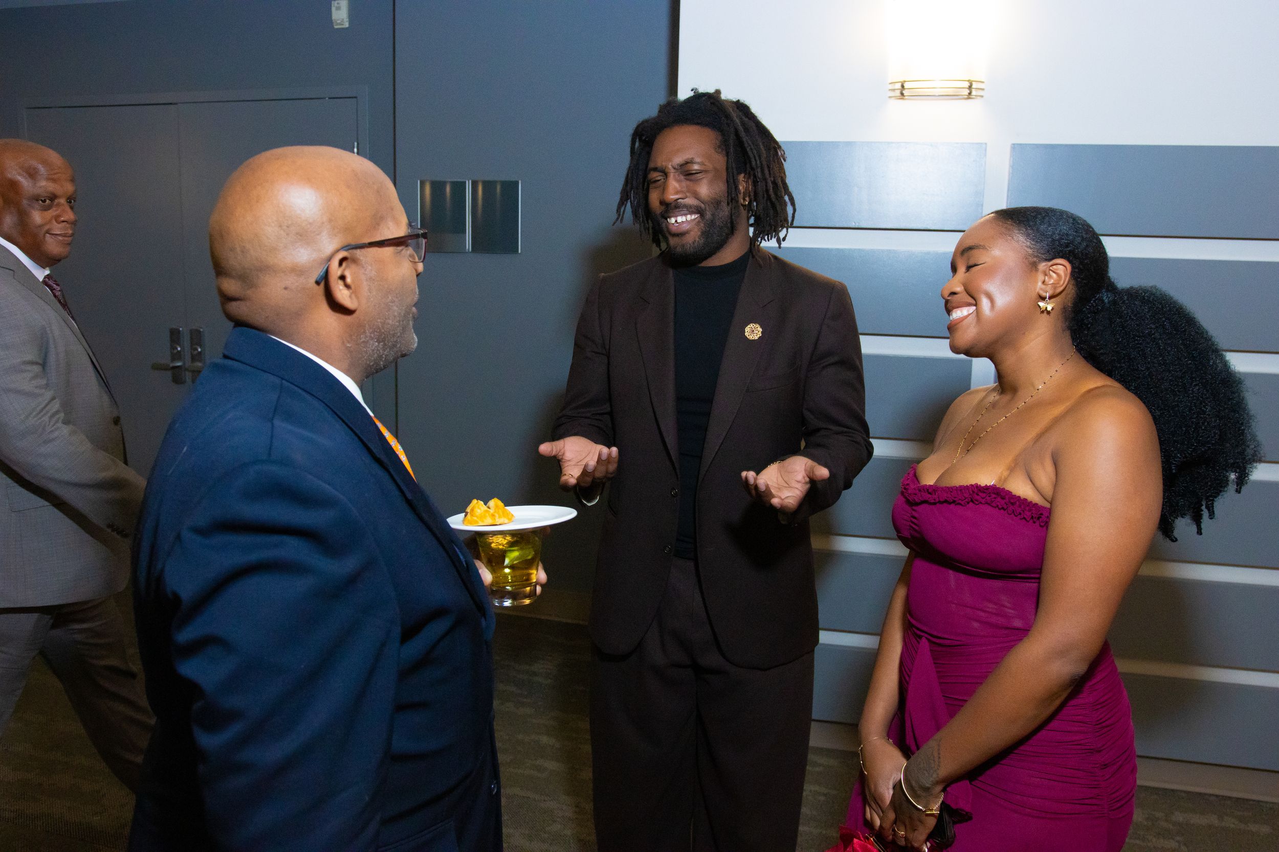 Three people in formal attire share a joyful conversation at an elegant evening social event.