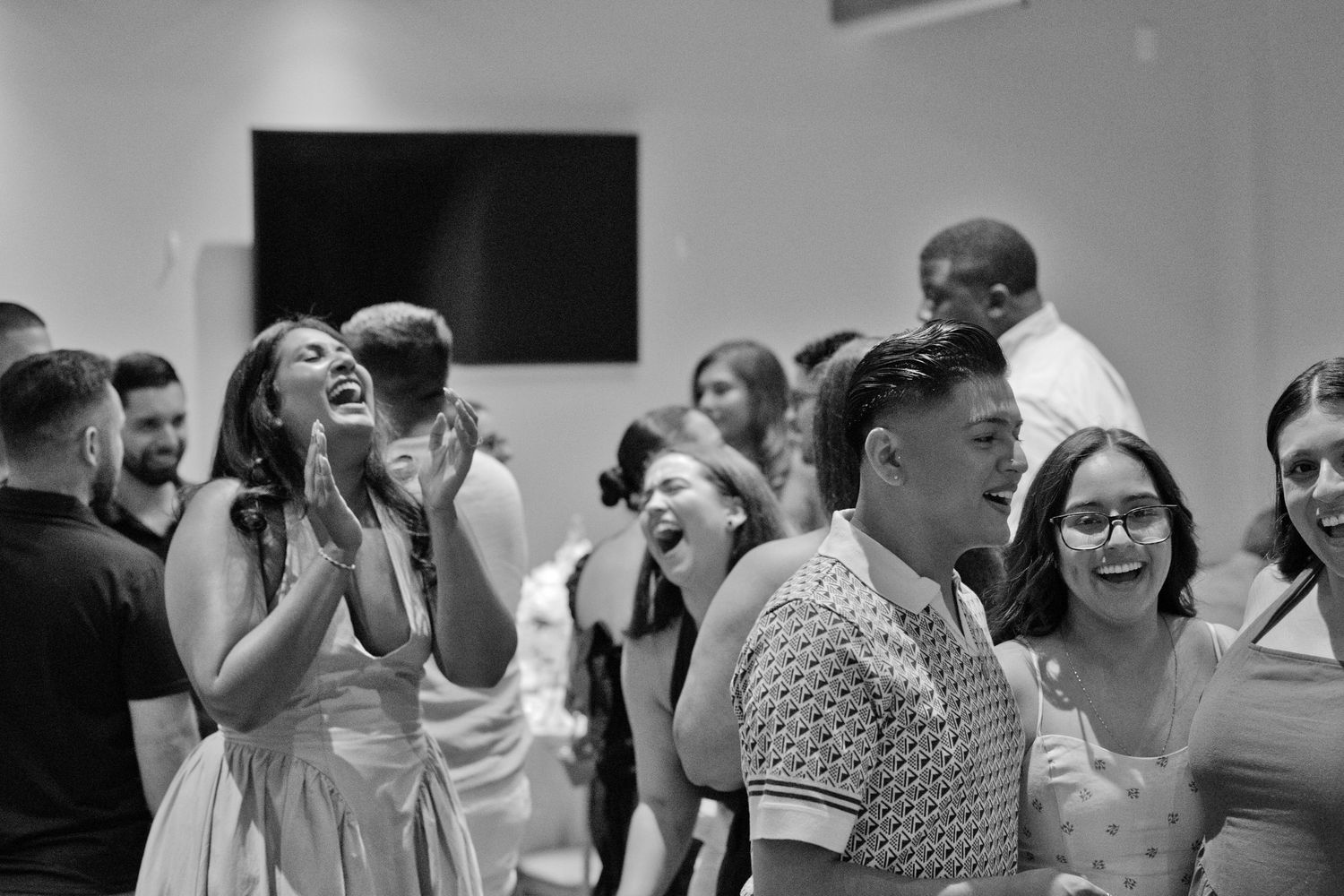 Black and white photo of laughing, clapping wedding guests enjoying a lively reception celebration together.