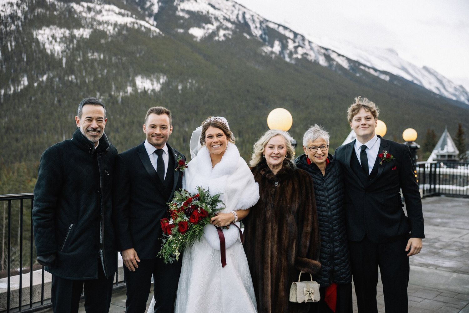 Smiling family group photo with the bride and groom at a Fairmont Banff Springs wedding, forested slopes behind