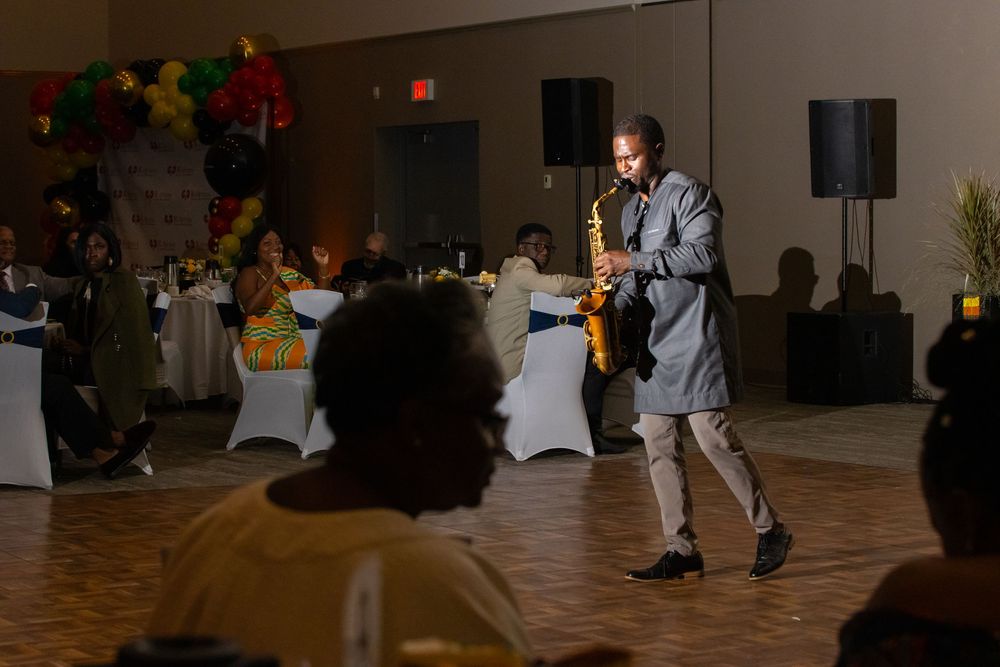 Saxophonist performing at an elegant banquet hall event with balloon decorations and seated guests.