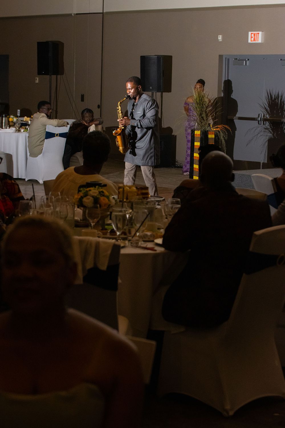 Saxophonist performing live at an elegant banquet hall dinner event with guests seated at round tables.