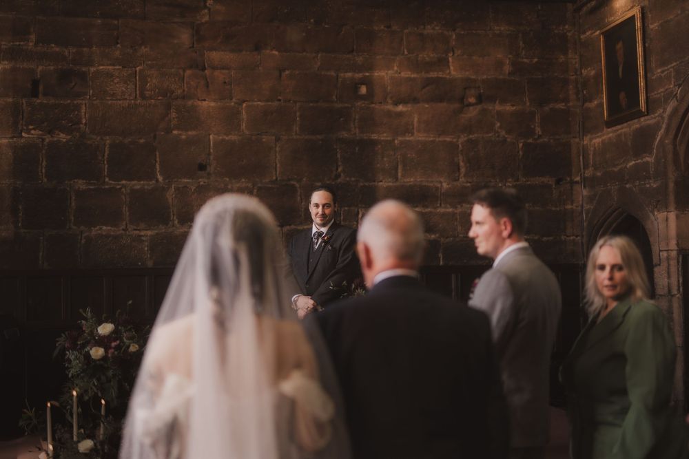 Bride walking down the aisle in a stone church toward the groom during a romantic wedding ceremony.