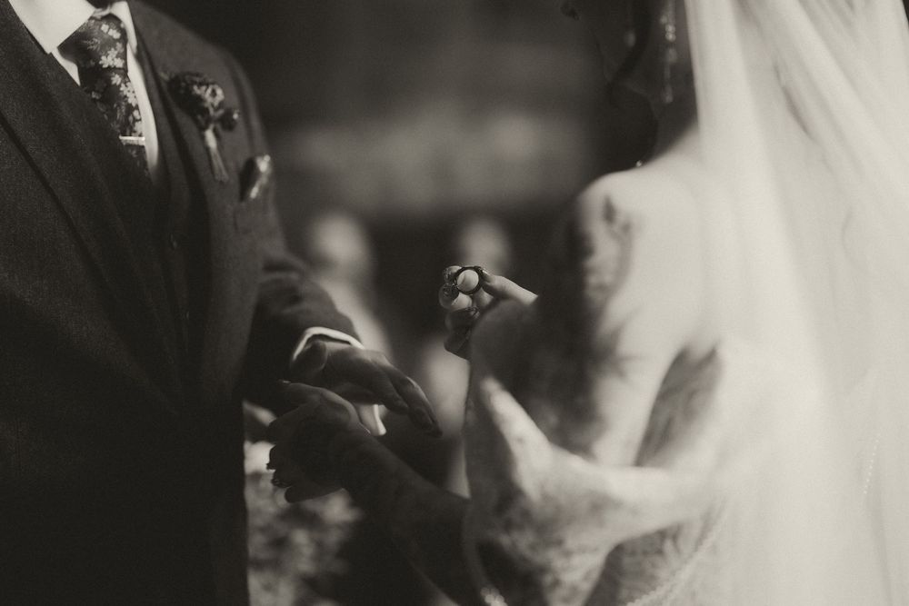 Black and white wedding photo of bride and groom exchanging rings during ceremony.
