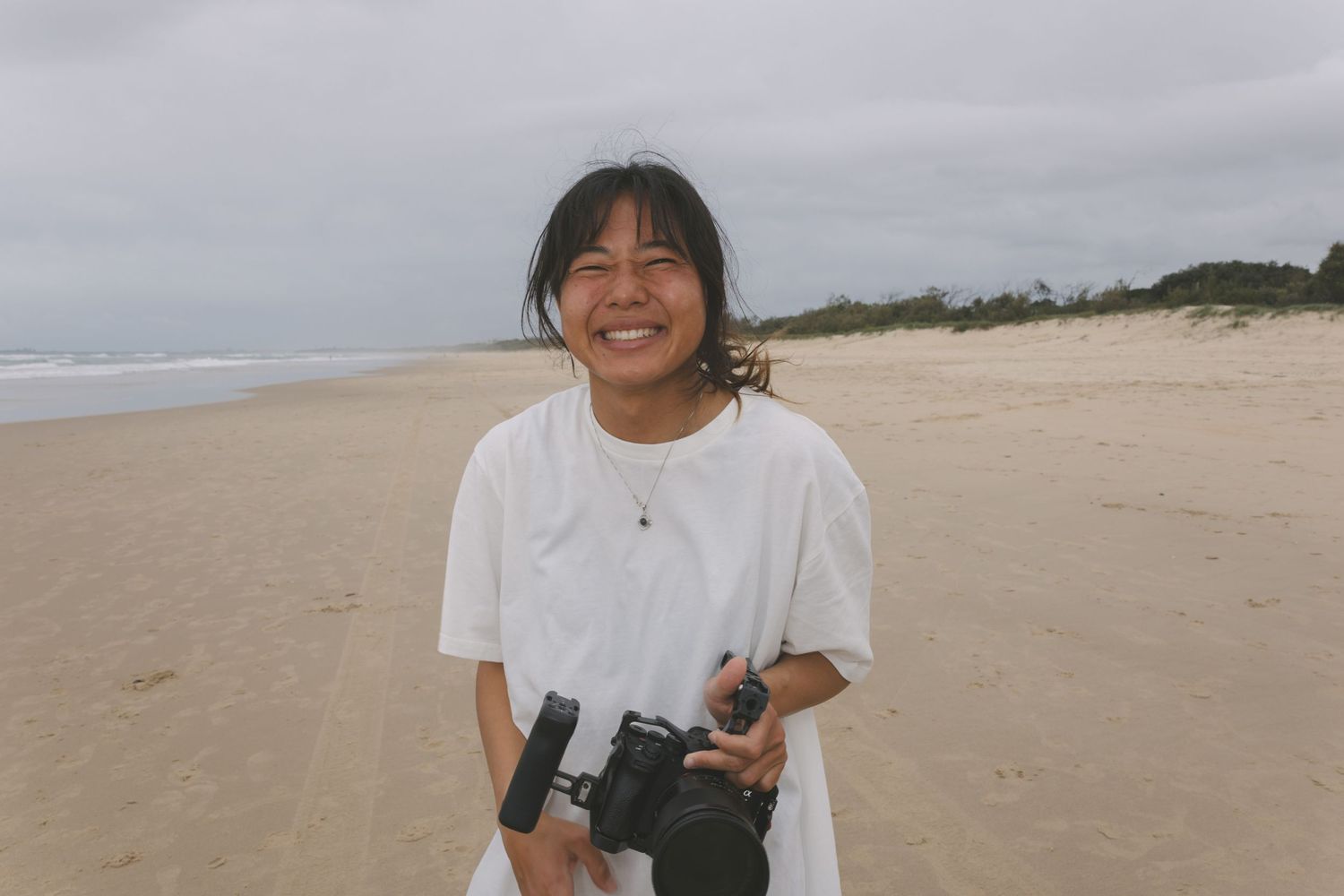 photo of female videographer Kanari with a video camera smiling into the camera on the beach on the sunshine coast, AUS.
