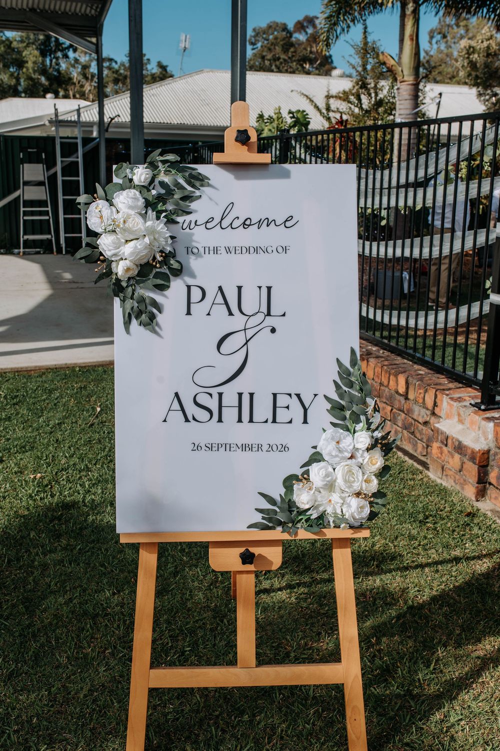 Elegant wedding welcome sign for Paul and Ashley on September 26, 2026, displayed on a wooden easel with white floral decor.