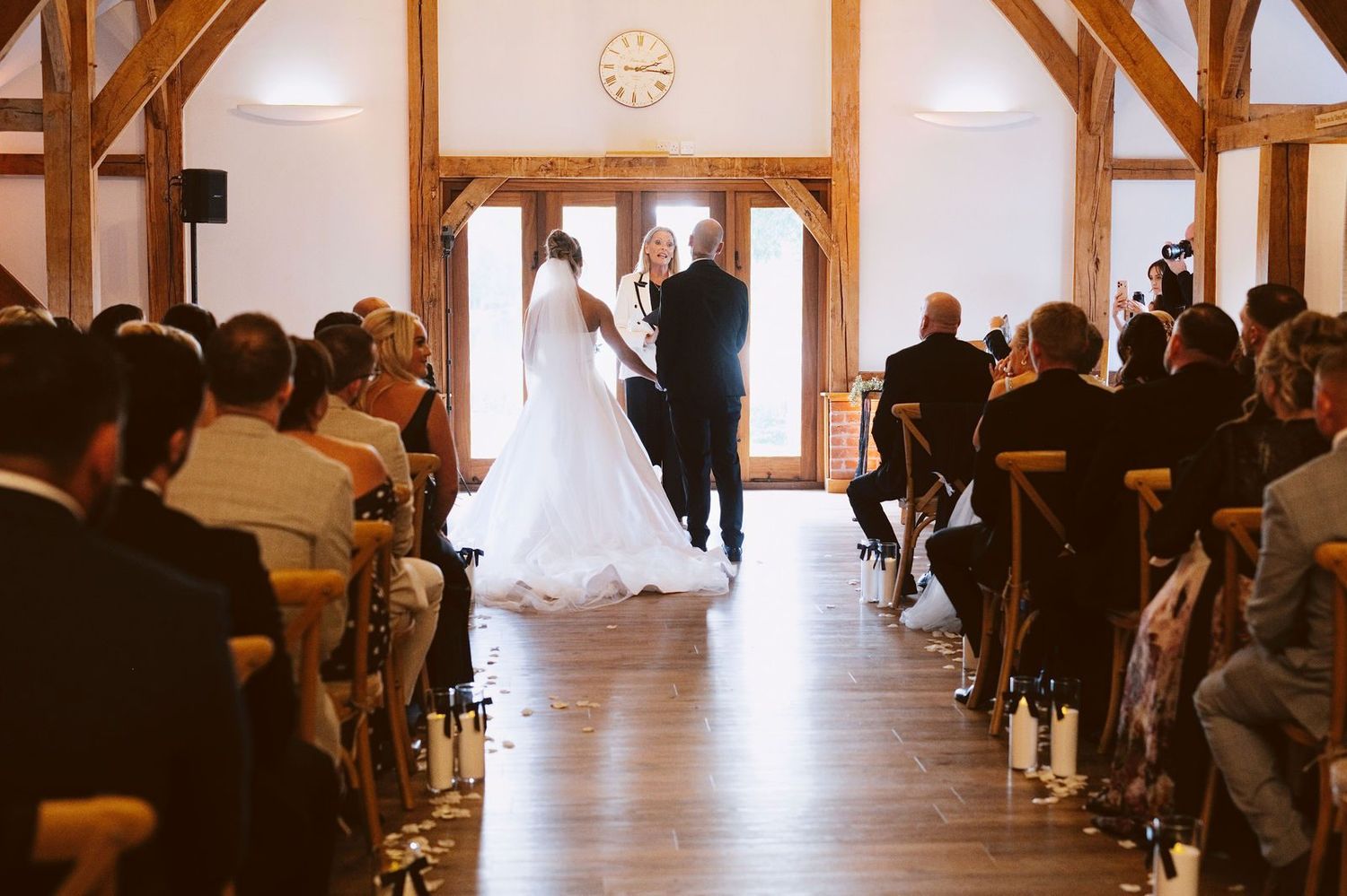 Sandhole Oak Barn wedding photography: looking down the Ceremony Barn aisle under oak trusses to the couple