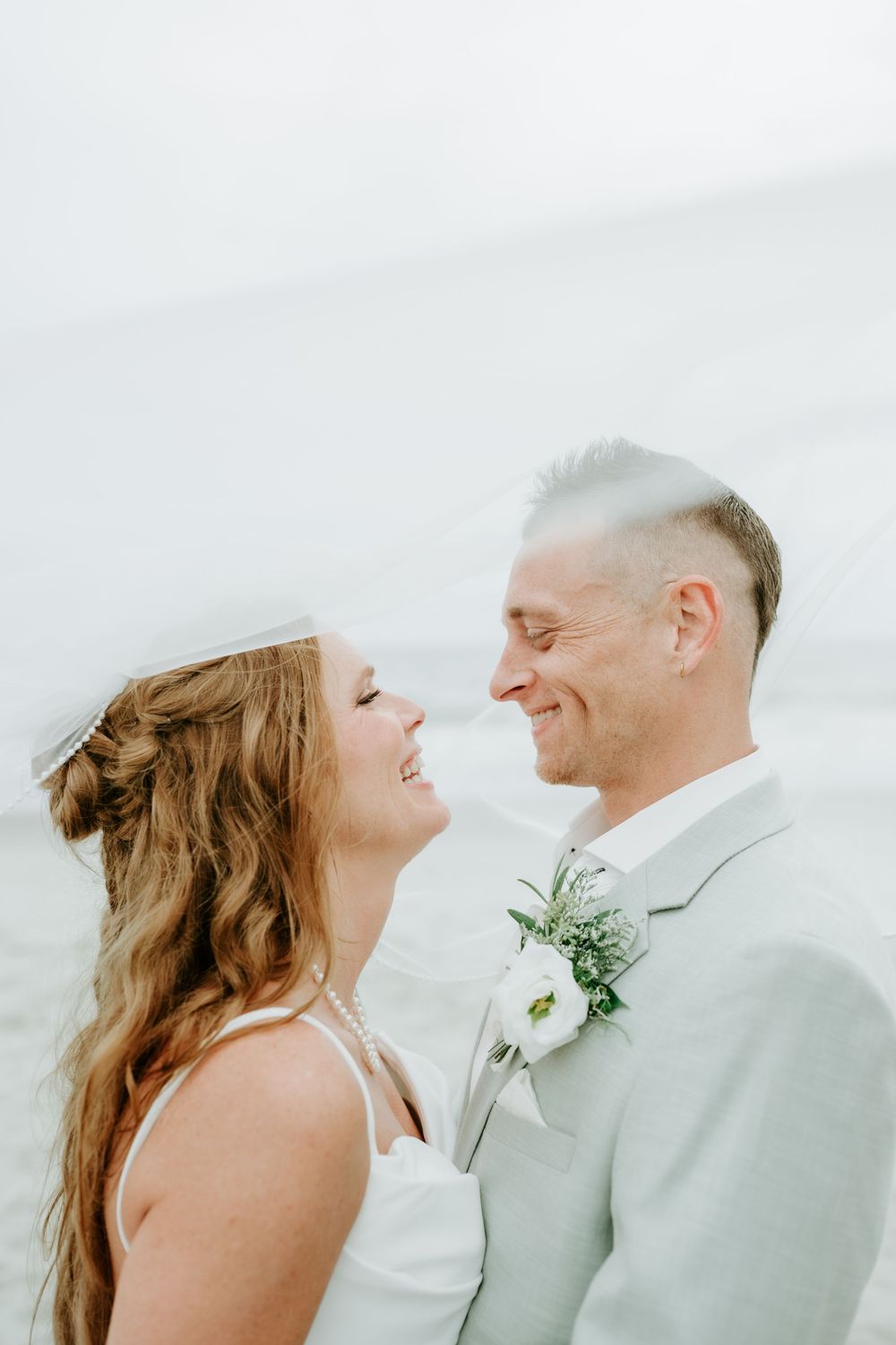 Bride and groom share a joyful moment smiling at each other during their beach wedding ceremony.