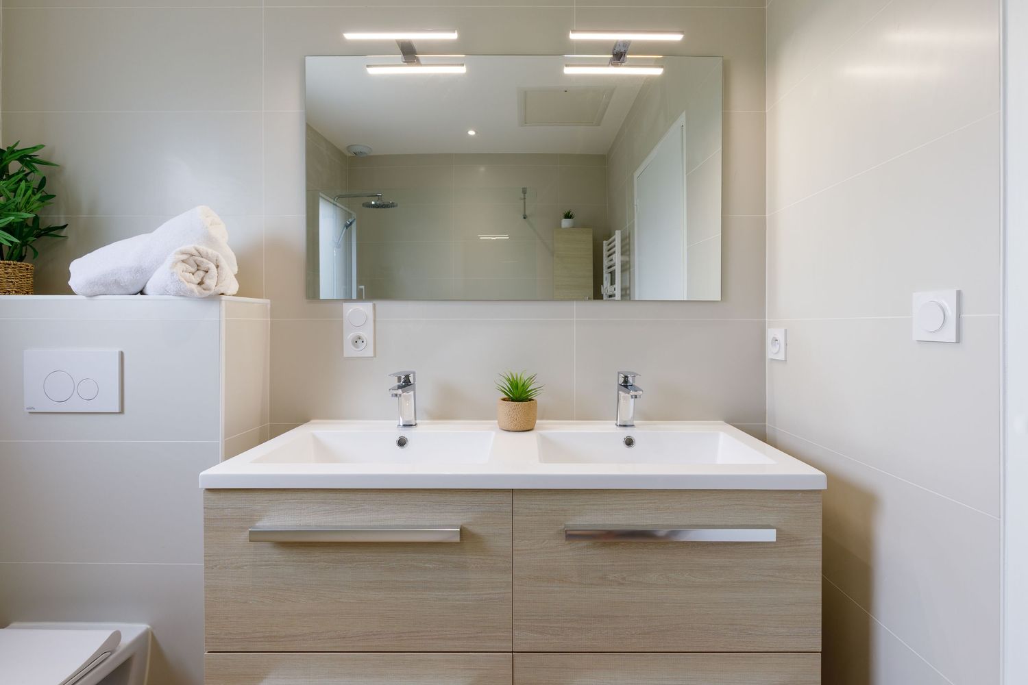 Meuble lavabo à double vasque, avec meuble en bois, grand miroir et robinetterie chromée, dans un style lumineux et minimaliste.