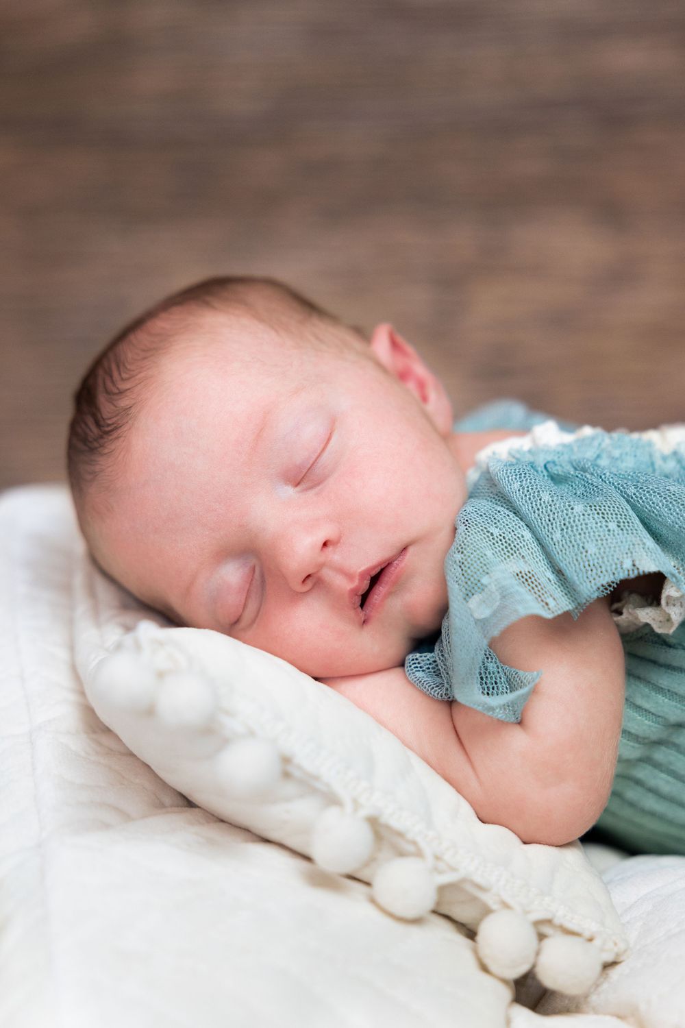 Peaceful newborn baby sleeping on white pillow wearing a soft teal knit outfit.