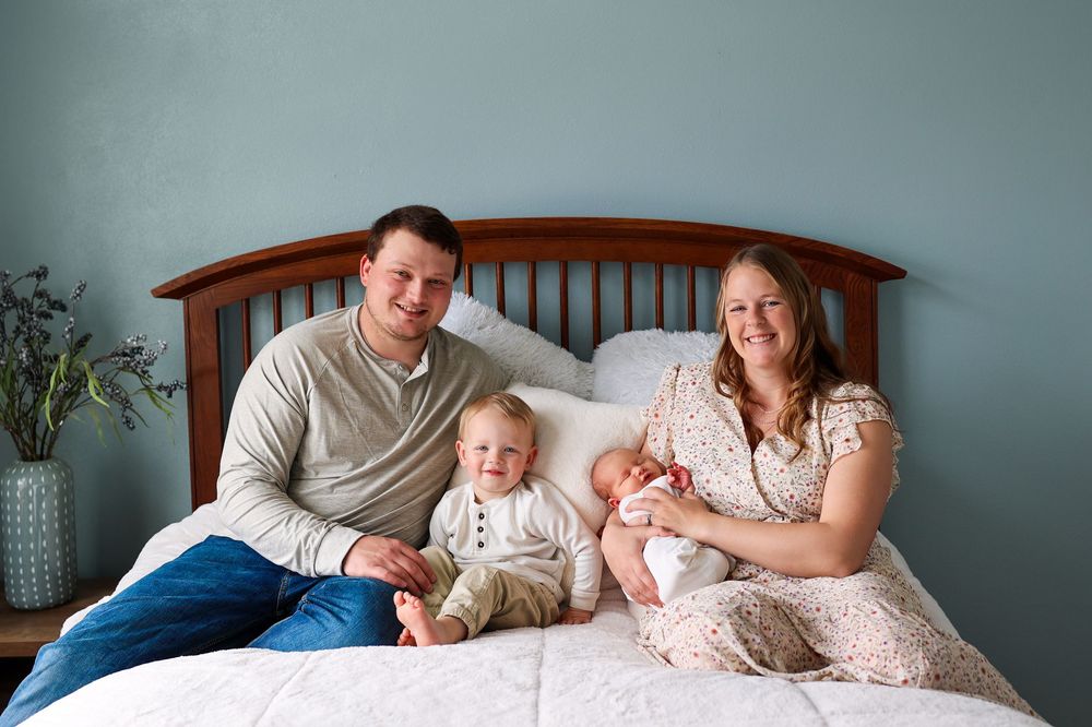 Happy family of four with newborn baby and toddler posing together on a bed.