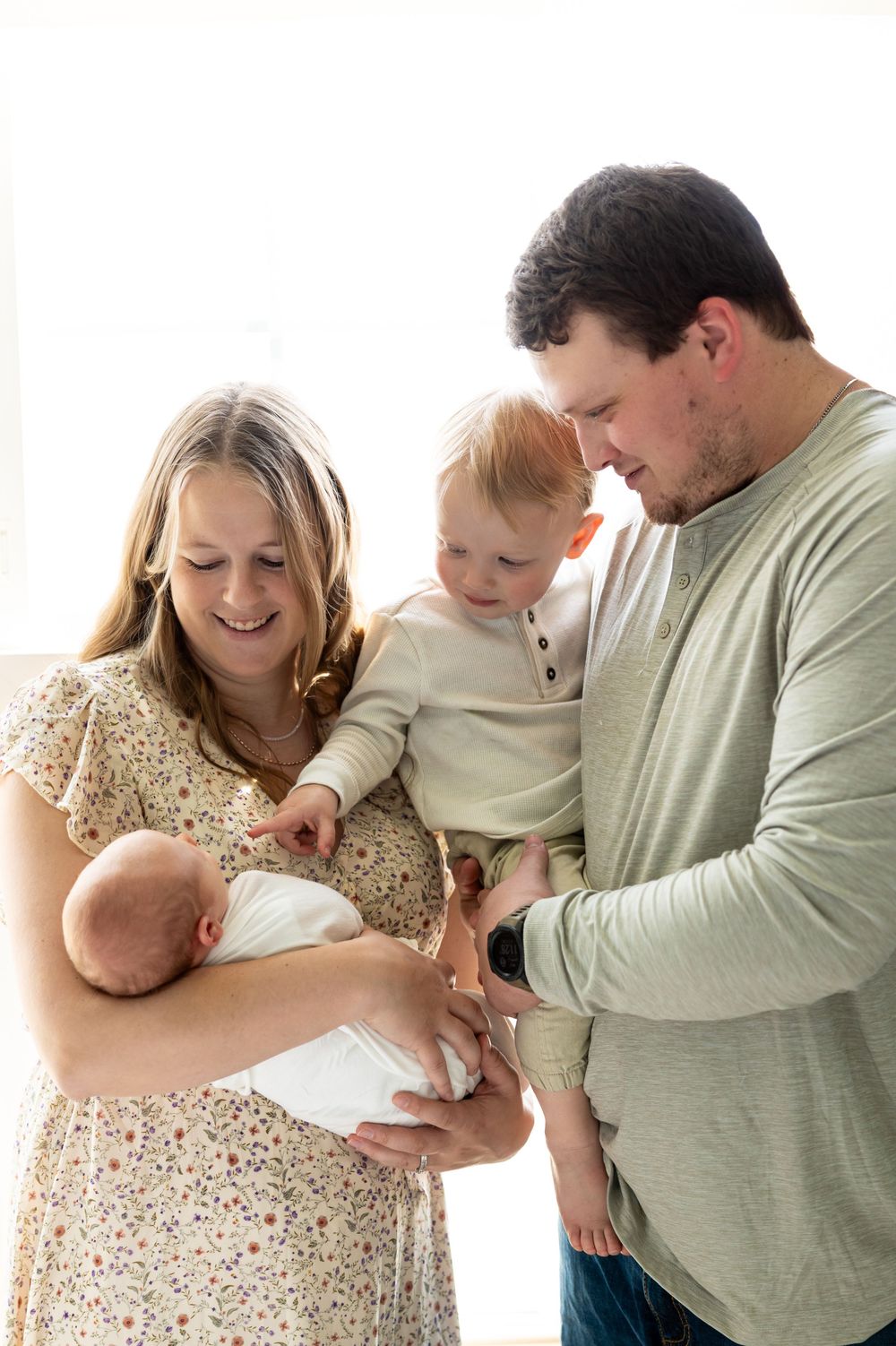 Parents and toddler admiring their newborn baby in a bright, light-filled room.