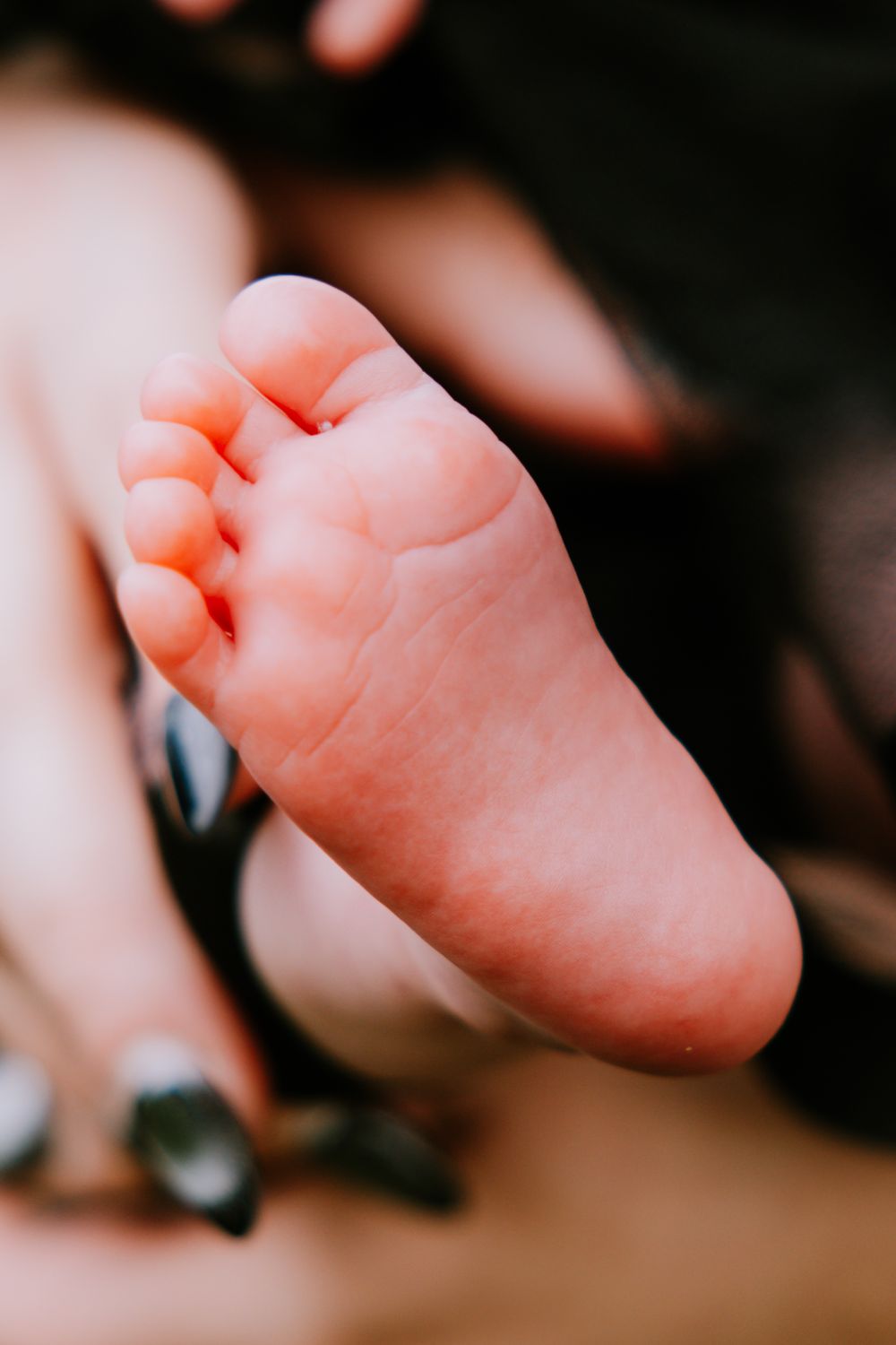 Close-up of a tiny newborn baby foot held gently by a parent with dark painted nails.
