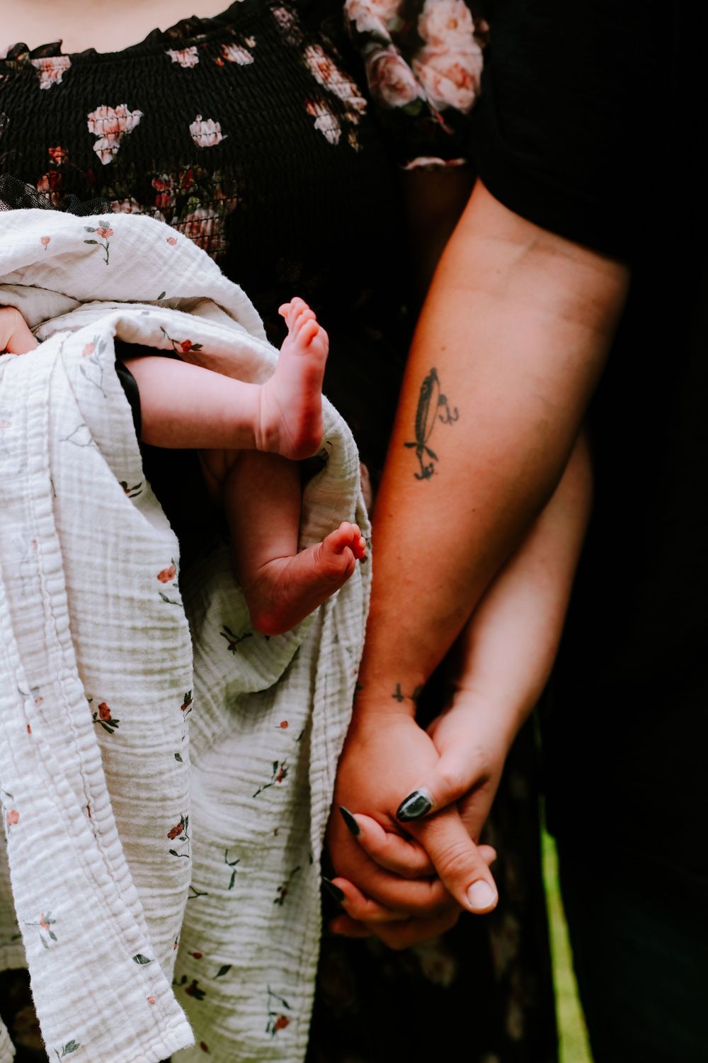 Parents holding a swaddled newborn in a floral blanket, father showing a fish tattoo on his forearm.