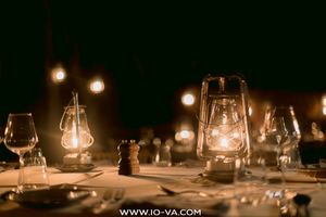 Glowing vintage lanterns, wine glasses, and a pepper mill on an elegantly set outdoor dinner table at night.