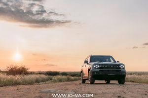 Ford Bronco Sport SUV parked on a dirt road in a grassy field at sunset, with a glowing orange sky and scattered clouds.