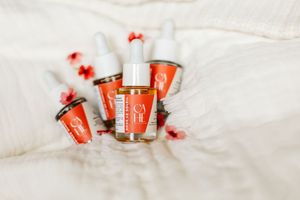 Huiles de soin Cahé Cosmetics répartis sur un drap blanc avec des petites fleurs aux tons roses