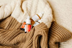 Huiles de soin Cahé Cosmetics disposées sur un pull d'hiver aux tons vert marron et blanc