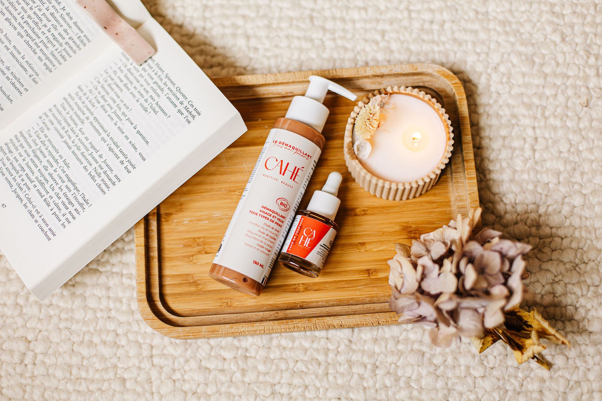 Produits de soin Cahe Cosmetics sur un plateau en bois avec une bougie et un livre ouvert