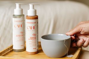 Produits Cahé Cosmetics posés près d'une tasse qu'une main humaine tient