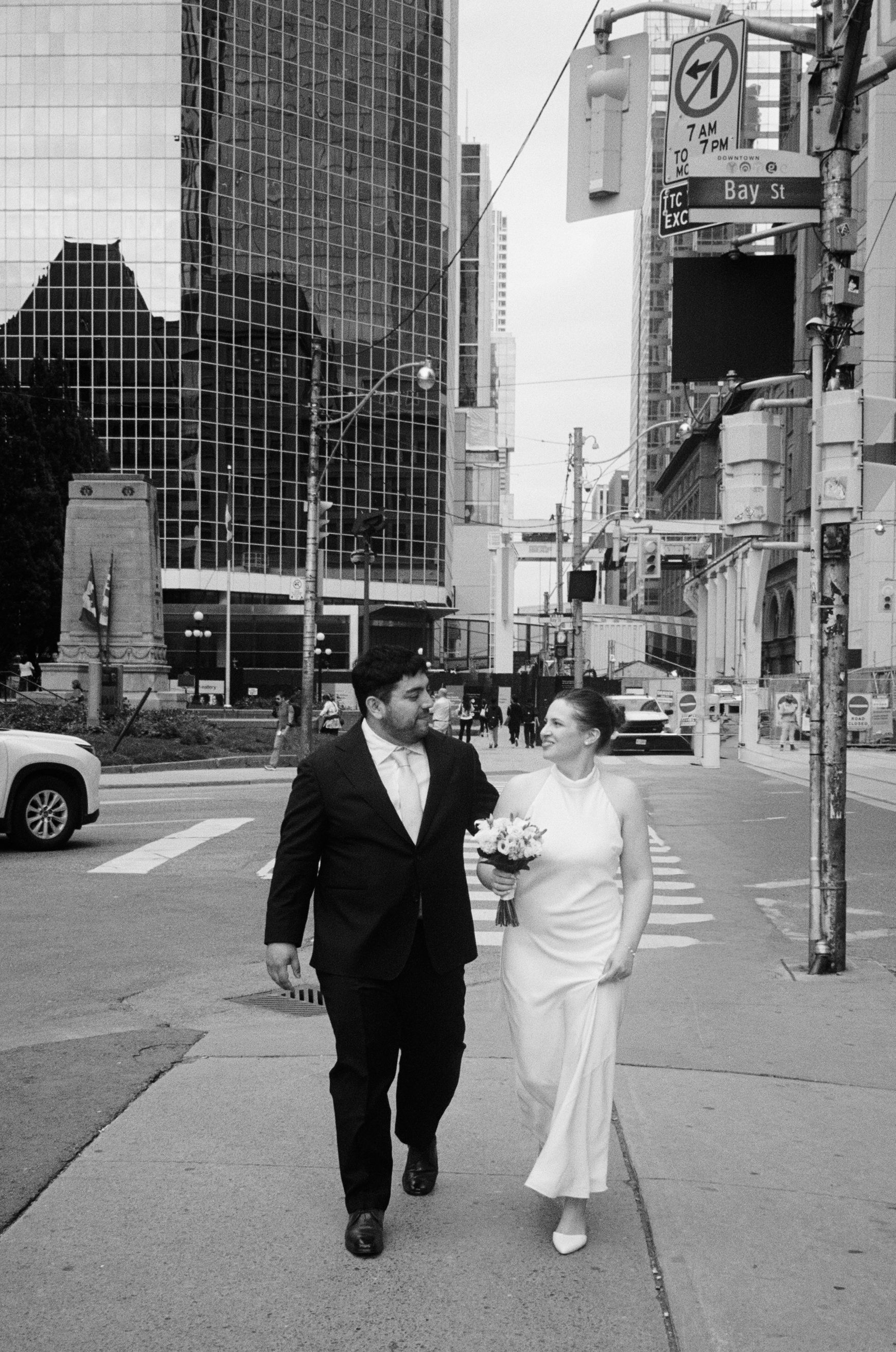 Bride and groom walking hand in hand on Bay Street in Toronto, black and white wedding photo.
