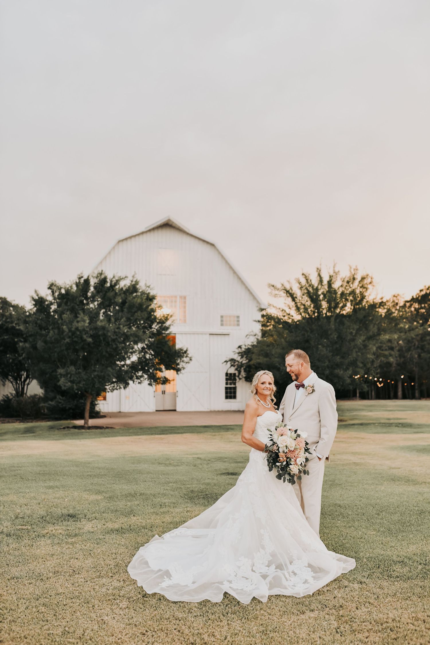Wide wedding portrait of bride and groom between the white barn and chapel at The White Sparrow